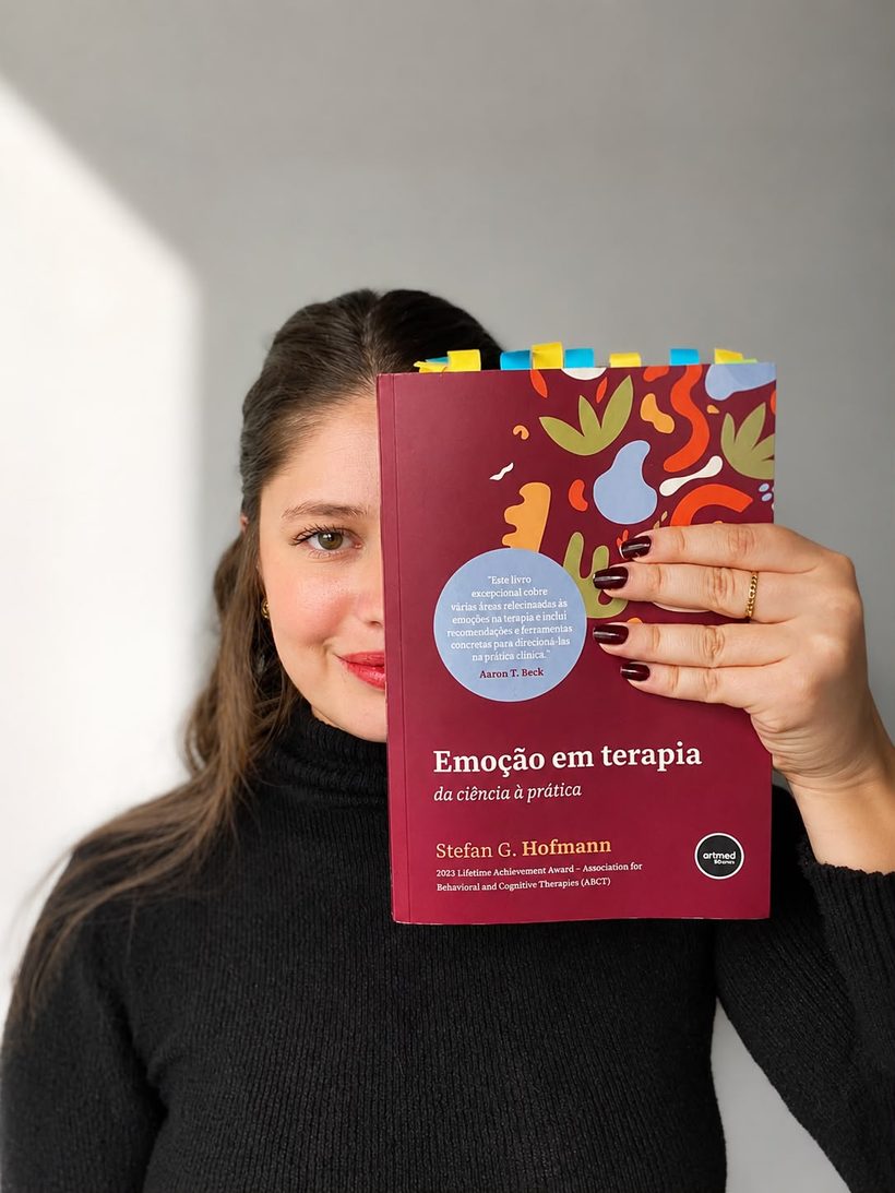 Sabryna Santos, psicóloga online para mulheres, segurando um livro sobre emoção em terapia